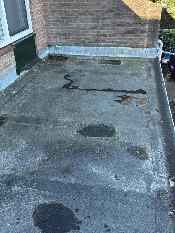 Een oud plat dak met plassen en waterschade, voordat MJB het vernieuwde